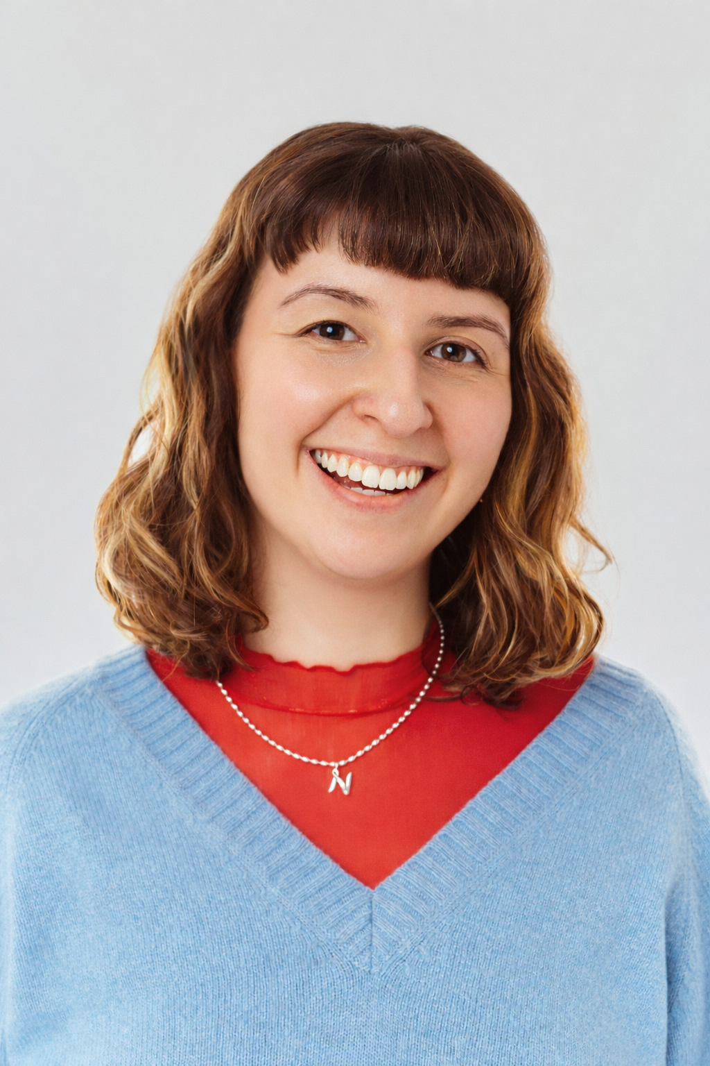 Natalie smiles at the camera in a red turtleneck and blue sweater.