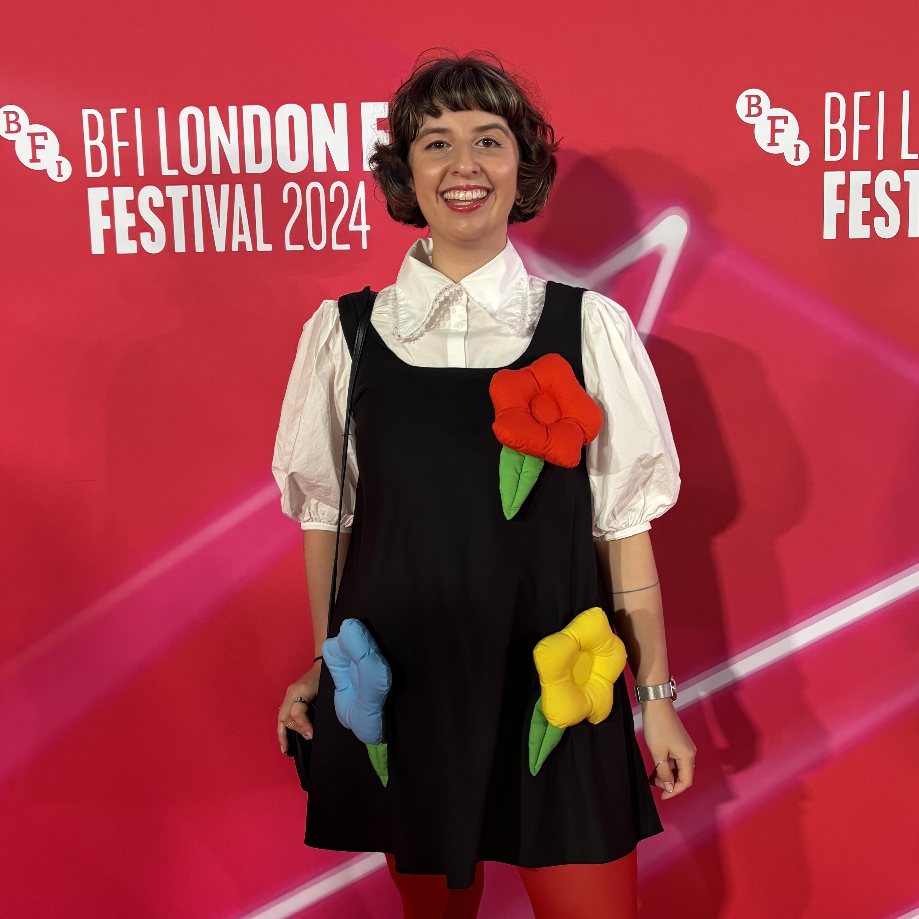 Natalie stands in front of signage for London Film Festival wearing a black dress with flowers